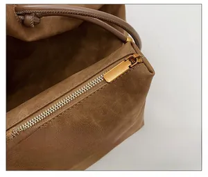 Detail of smooth gold zipper and leather drawstring on brown suede tote bag
