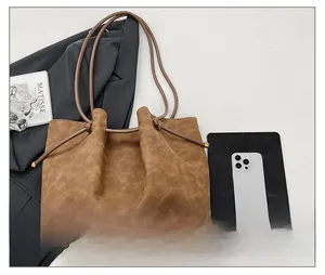 Detail of brown faux suede tote bag featuring drawstring closure and gold metal aglets