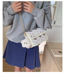 Detail of cartoon cat print on cream crossbody bag with chain strap and plush star charm
