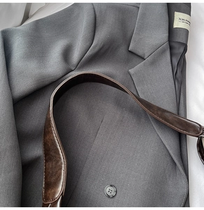 Vue détaillée de la bandoulière en cuir marron sur le tissu gris d'un blazer chic
