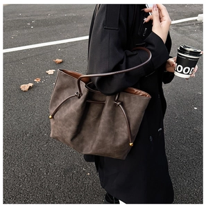 Detail of dark brown tote bag showing side leather drawstring and gold ball ornament