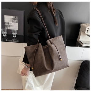 Detail of dark brown leather tote bag with pleated design and gold ball drawstring accents