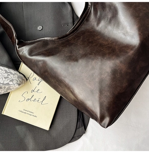 Détail d'un sac cabas en cuir souple marron foncé sur fond de costume et livre vintage