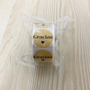 Detail of round kraft paper stickers with black Gracias text and heart on a roll