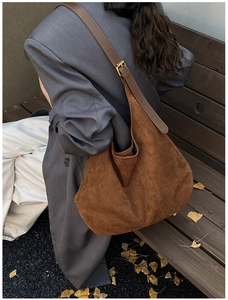 Detail of dark brown suede tote bag featuring a leather strap on a fall outdoor background