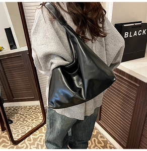 Gros plan d'un grand sac hobo en similicuir noir brillant avec une large bandoulière souple