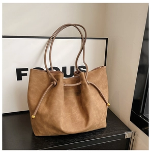 Detail of brown faux suede tote bag with drawstring tassel and gold bead accents