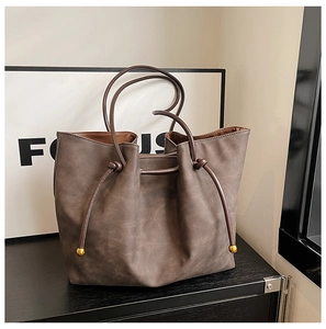 Detail of coffee brown suede tote bag featuring a drawstring closure and gold ball metal tips