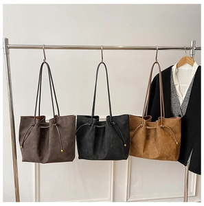 Three minimalist suede tote bags in brown, black and tan with drawstring gold beads