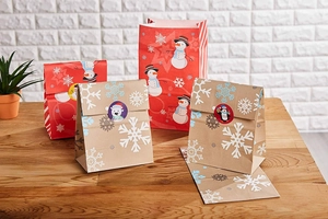 Festive Christmas paper gift bags with snowman and snowflake designs on a wooden table