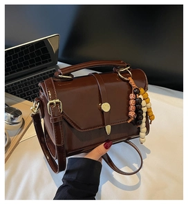 Detail of dark brown glossy leather handbag with colorful wooden bead tassel decoration