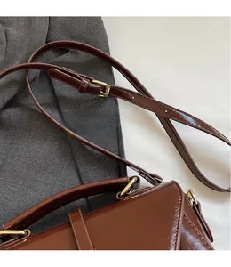 Detail of adjustable leather strap and golden hardware on a brown glossy handbag