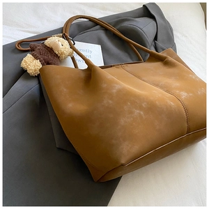Détail du sac cabas en daim caramel avec breloque ours sur une veste de blazer grise