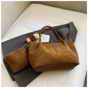 Détail d'un grand sac cabas en daim marron avec pochette et porte-clés ours sur lit blanc