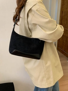 Minimalist black underarm bag with suede and leather patchwork, worn by a model in a bright room