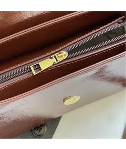 Detail of brown leather handbag featuring a glossy golden metal zipper and smooth texture