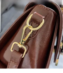 Detail showing high-shine brown oil wax leather texture and gold metal hook on shoulder bag