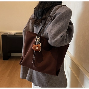 Detail einer dunkelbraunen Wildleder-Tote-Bag mit einem süßen Plüschbären-Anhänger an der Seite