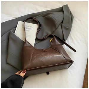 Dark brown faux leather Hobo bag on grey blazer and white book with golden zipper