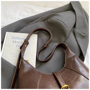Detail of a deep brown hobo bag with adjustable strap and gold hardware on grey suit