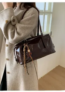 Detail of a dark brown glossy underarm bag with silver zipper and a cute bear charm