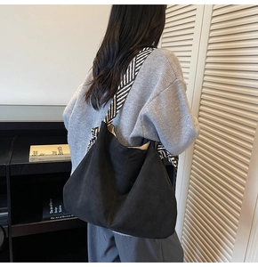 Detail of a large black suede hobo bag with a black and white striped ribbon strap