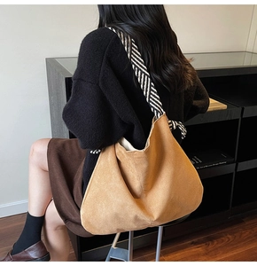 Detail of brown suede tote bag featuring a contrasting black and white woven shoulder strap