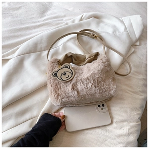 Vue détaillée du sac bandoulière en peluche beige avec poignée plissée et breloque ours