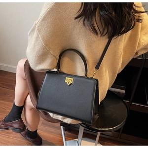 Model view of black leather top-handle bag with gold clasp and crossbody strap