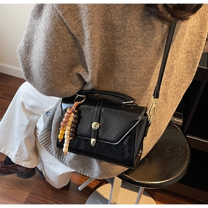 Close-up of black pleated leather crossbody bag with colorful ethnic beaded charm and gold hardware