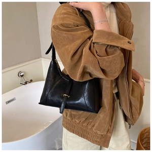Close-up of black glossy leather baguette bag with gold buckle on model's shoulder