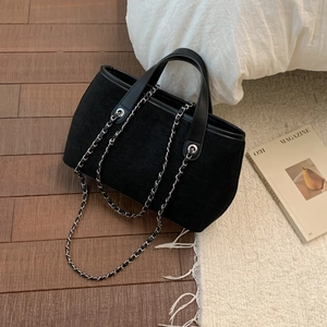 Detail of minimalist black suede tote bag with leather handles and silver chain on a rug