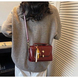 Detail of a burgundy glossy crossbody bag with vintage wooden beads on a model