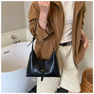 Close-up of black glossy leather shoulder bag featuring a decorative gold buckle detail