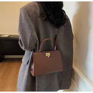 Detail showing a dark brown leather vintage satchel bag with a gold shield-shaped lock