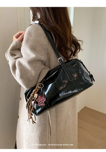 Detailed view of a black glossy oil wax leather Boston bag with a leopard bear charm