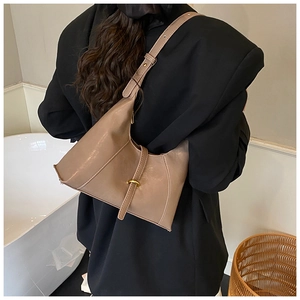 Detail view of a tan leather baguette bag with gold buckle on a model shoulder