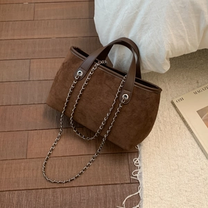 Detail of a brown faux suede tote bag featuring sleek leather trim and metallic chain strap