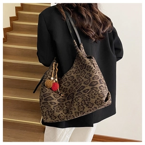 Detail of leopard print tote bag with plush pom-poms on a black shoulder strap