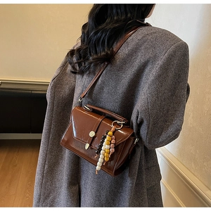 Brown glossy leather crossbody bag with colorful bead charm on a grey wool coat