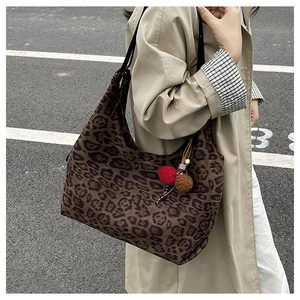 Close-up of leopard print tote bag with plush pom-pom charm and black adjustable strap