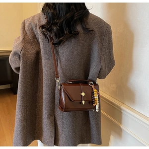 Detail of dark brown glossy leather bag with gold buckle and wooden bead charm