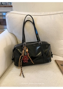 Detail of glossy black leather retro bowling bag with red leopard bear charm on sofa