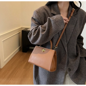 Detail of vintage brown leather tote bag with gold metal lock and gray blazer styling
