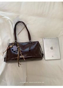 Detail of dark brown vintage oil wax leather handbag with charms on white fabric