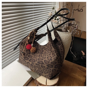 Detail of leopard print tote bag with red plush charms and leather shoulder strap