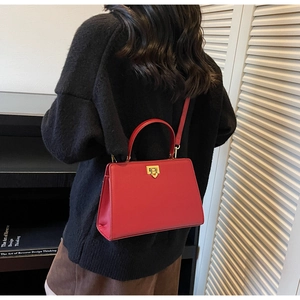 Detail of red leather crossbody bag featuring a golden metal twist lock and sturdy handle