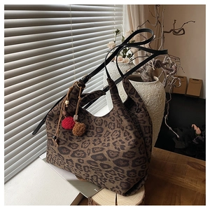 Detail of leopard print canvas tote bag with black leather straps and pompom charm