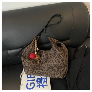 Detail view of leopard print canvas tote bag with black leather strap and pompom charm