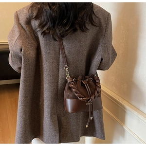 Detail of dark brown leather bucket bag with drawstring closure and woven handle